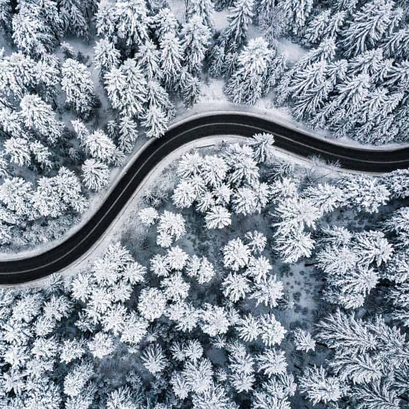 Curvy windy road in snow covered forest, top down aerial view.